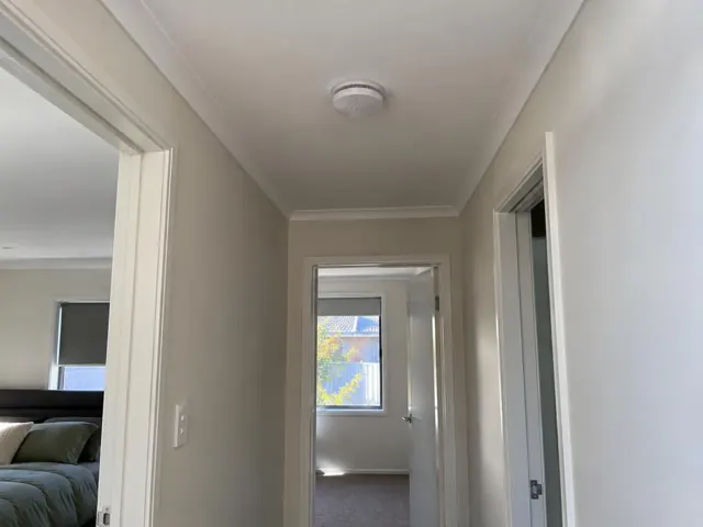 Ceiling smoke alarm in a painted hallway with doorways and bedroom view in Newcastle